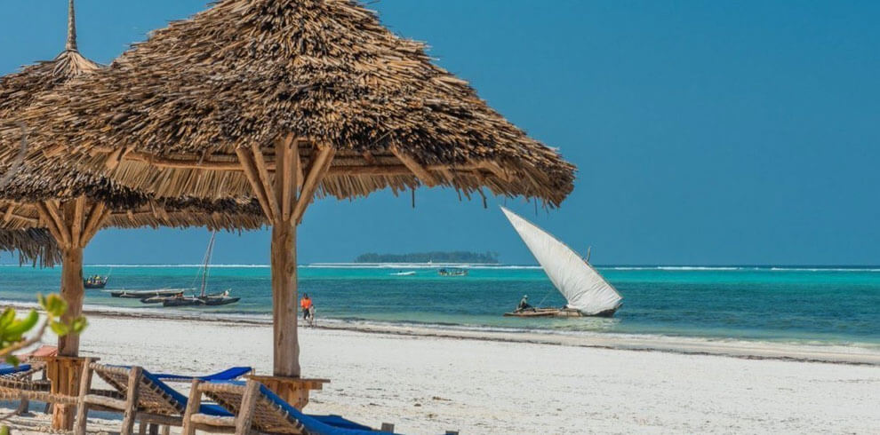 a beach with a straw umbrella and a boat on the water